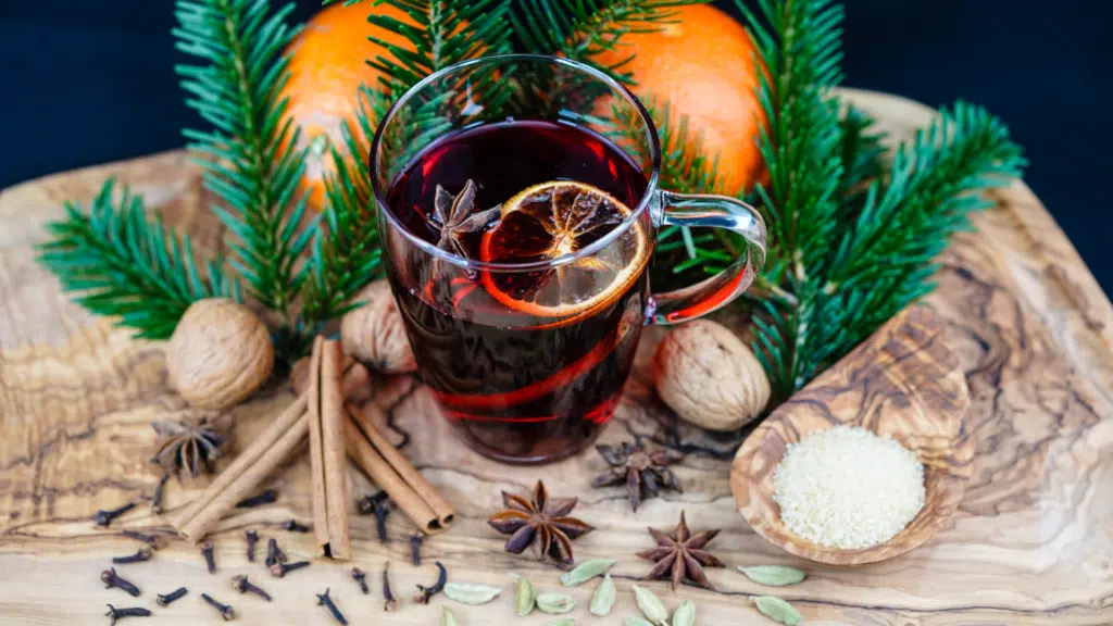 Pot of Glühwein gently simmering on top of the wood table with visible spices and citrus floating on top.