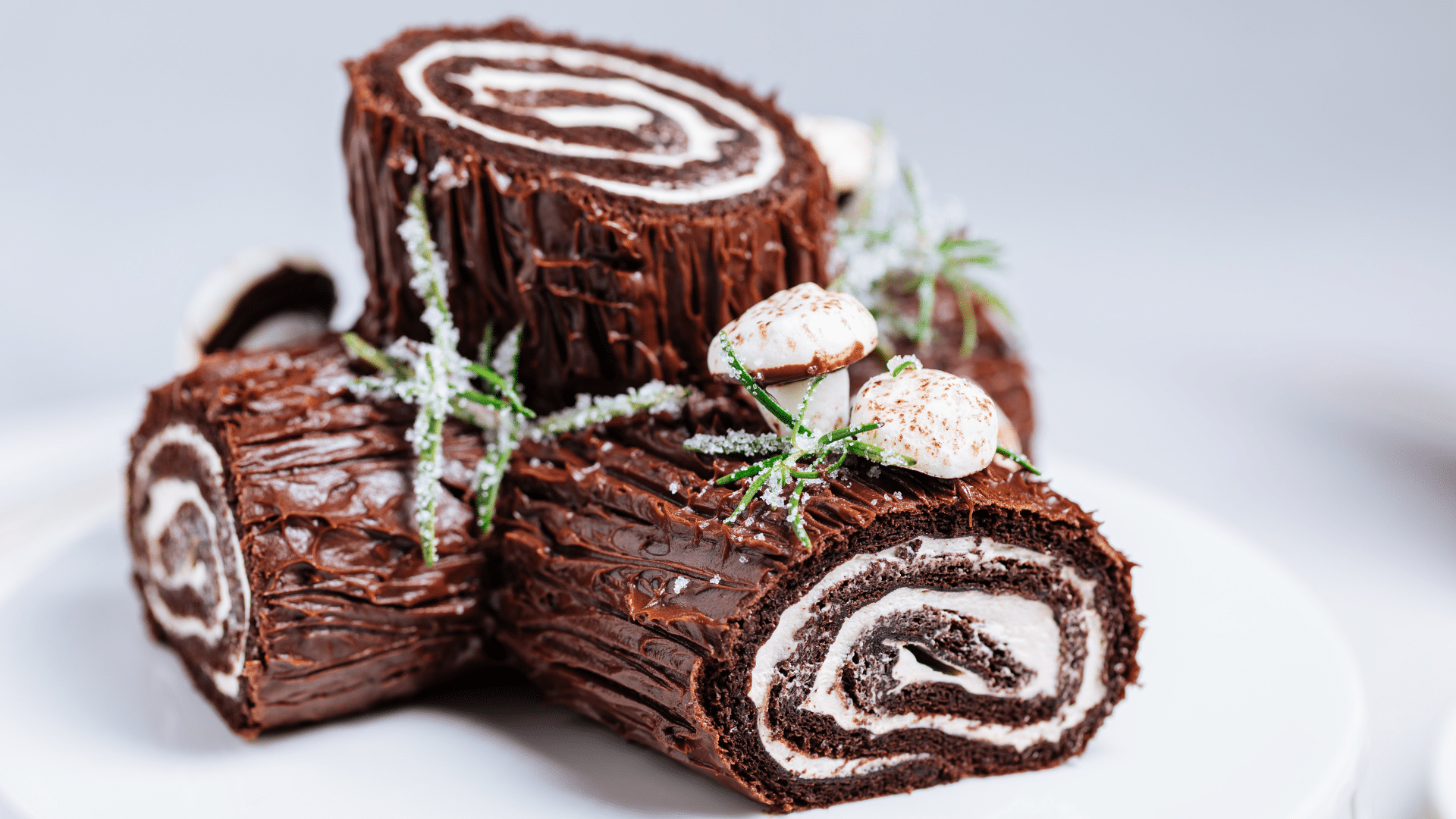Chocolate Bûche de Noël cake shaped like a festive Yule log, decorated with swirled buttercream, powdered sugar, and small holiday accents.