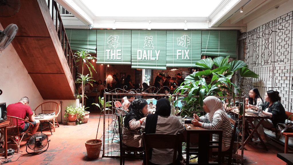 Entrance of The Daily Fix Café on Jonker Street Melaka, hidden behind a souvenir shop with rustic signage and traditional shophouse architecture.