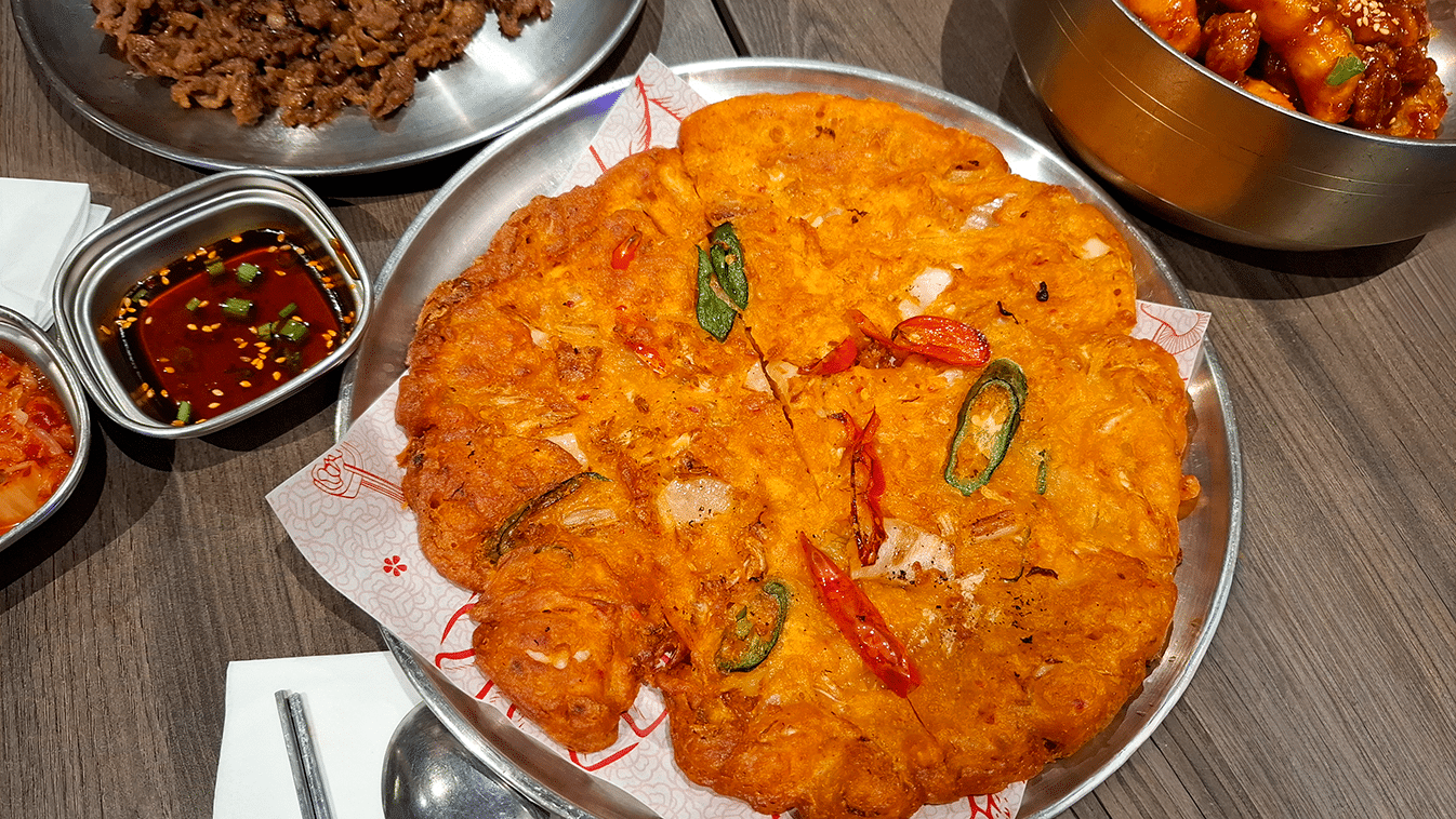 Crispy golden-brown kimchi pancake served on a plate, showing crunchy edges and soft chewy interior.